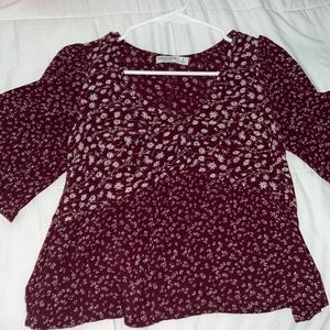 Burgundy floral top, with low cut in the front, sleeves flare.